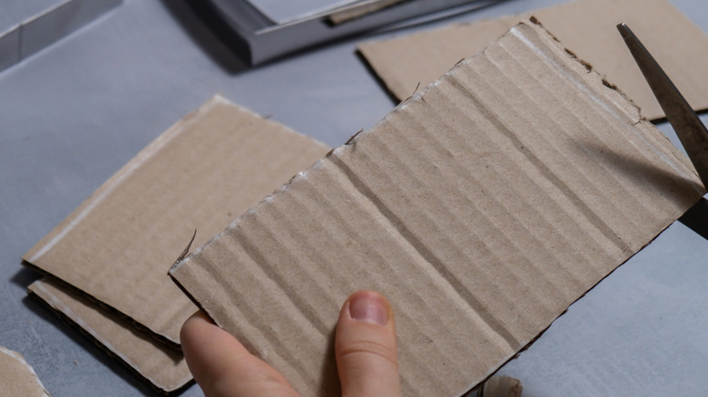 Light skinned hands hold and cut a piece of cardboard.