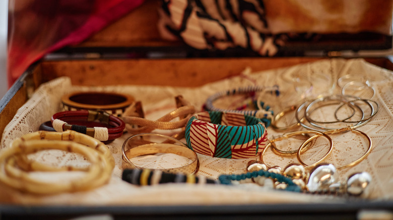 Various bangles and bracelets of different colors adnd metals laid out on a lace cloth