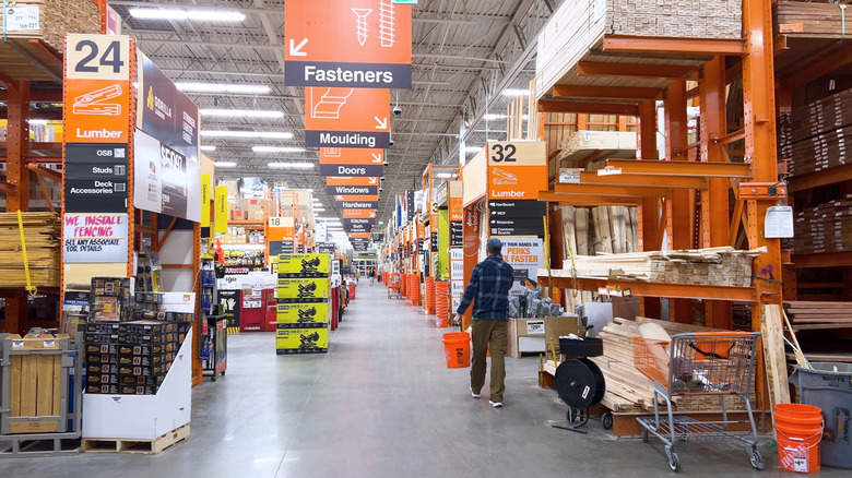 A man carries an orange gallon bucket as he walks the aisles of a hardware store.