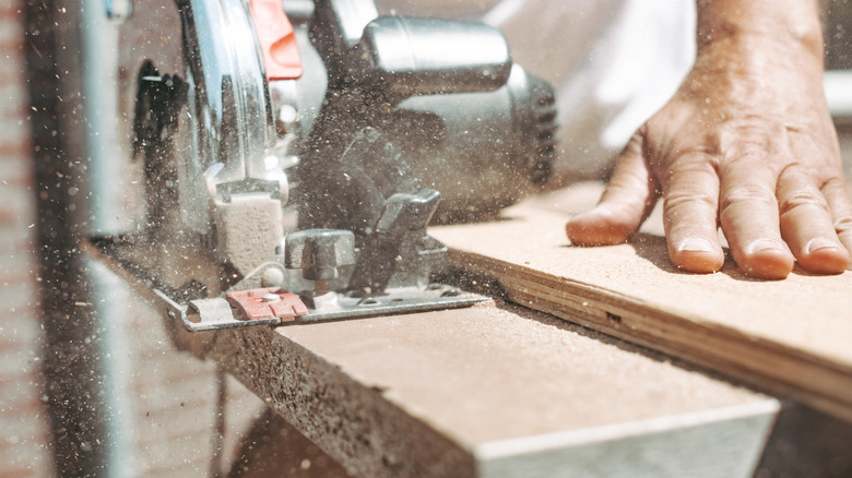 A hand holds a board as it's cut by a circular saw.