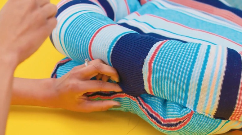 Hands sewing the stuffed arms of a sweater to the body