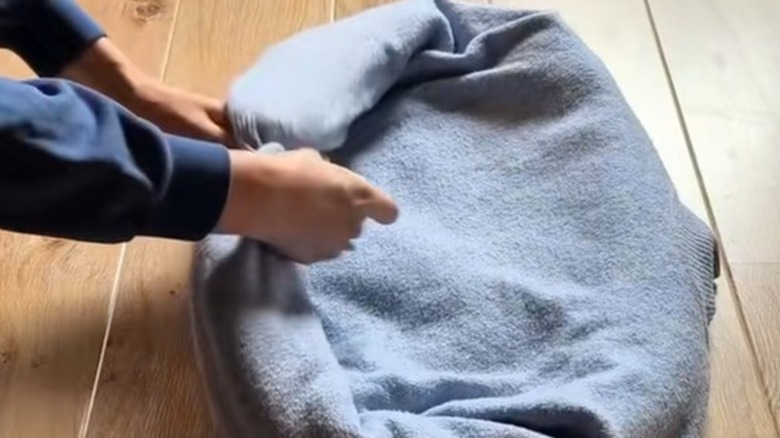 Hands tying up two arms of a stuffed blue sweater