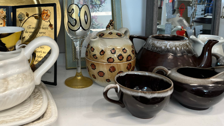Teapots and other dinnerware and décor on a display shelf in a thrift store.