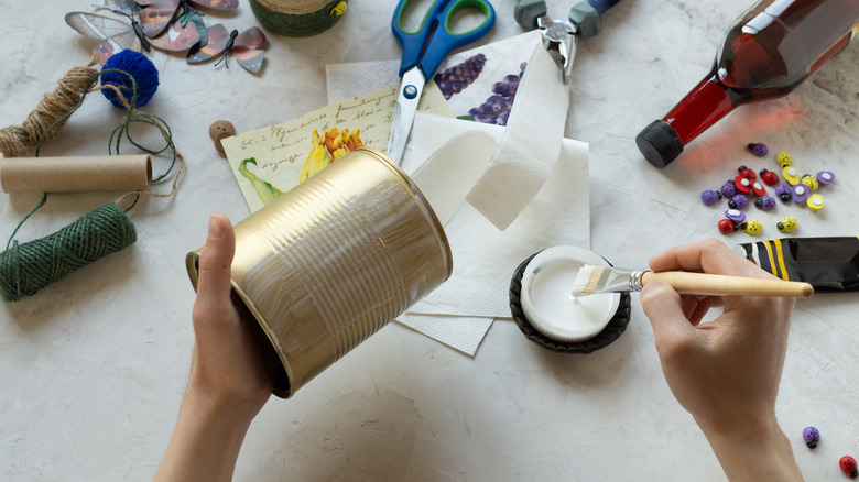 Person brushing Modge Podge on tin can for DIY