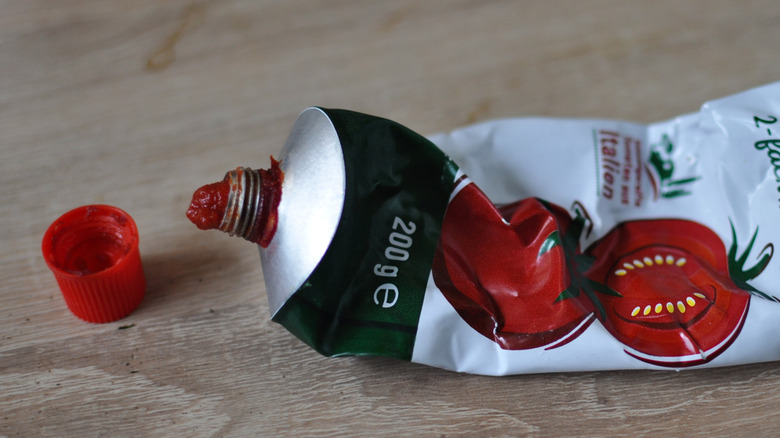 Crinkled tomato paste tube on a wood table next to its cap