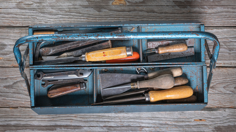 An old blue metal toolbox filled with rusty tools sitting on a wooden table