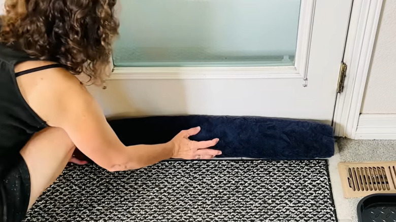 Person placing rolled towel at bottom of door