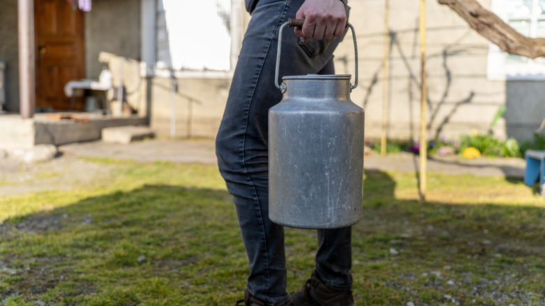 someone carries an old aluminum milk can
