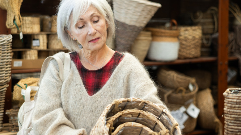 A woman looks at a stack of wicker baskets she's holding in her hand while shopping in a store.