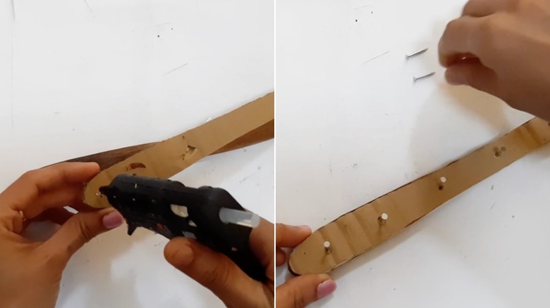 Hands glue a piece of cardboard and some nails to the handle of a wooden spatula.