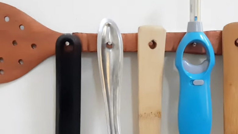 Wooden spoon transformed into a wall rack with utensils hanging.