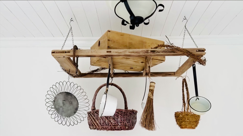 The finished hanging rack made from a window frame is shown with cooking pots, baskets, and rustic objects.