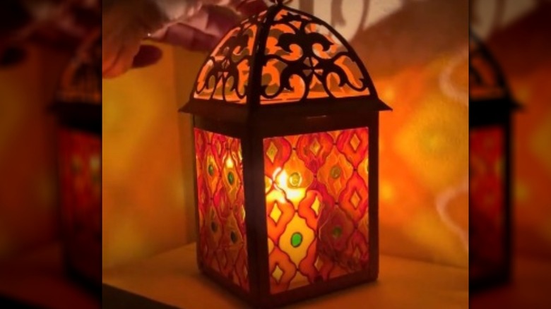 A colorful hand-painted lantern with lit candle inside.