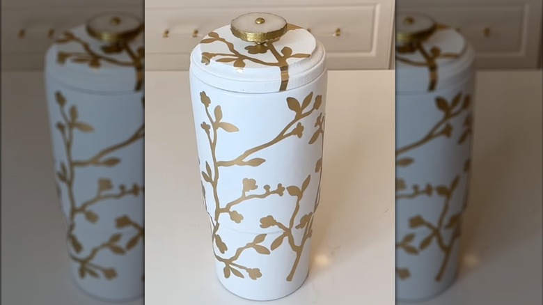 A white vase with lid is covered in gold, decorative vines