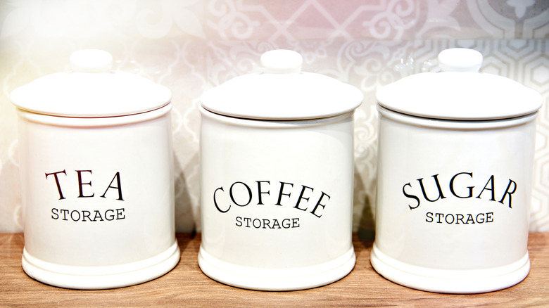 Three white ceramic kitchen canisters, labeled for Tea, Coffee, and Sugar.