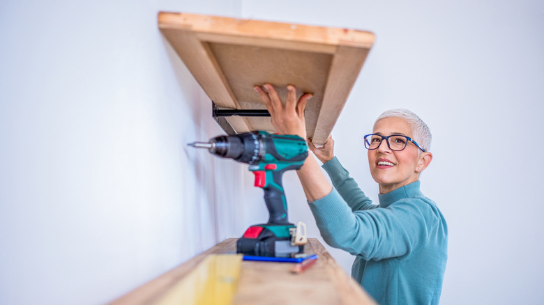 Woman installing wooden floating shelves on wall.