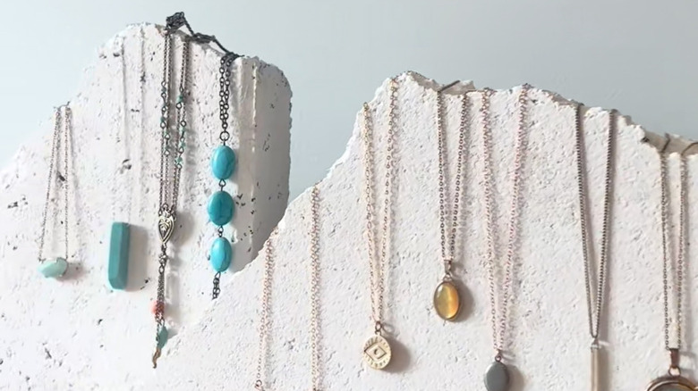 Several broken paving slabs being used as jewelry holders, with various necklaces draped over top of the jagged edges