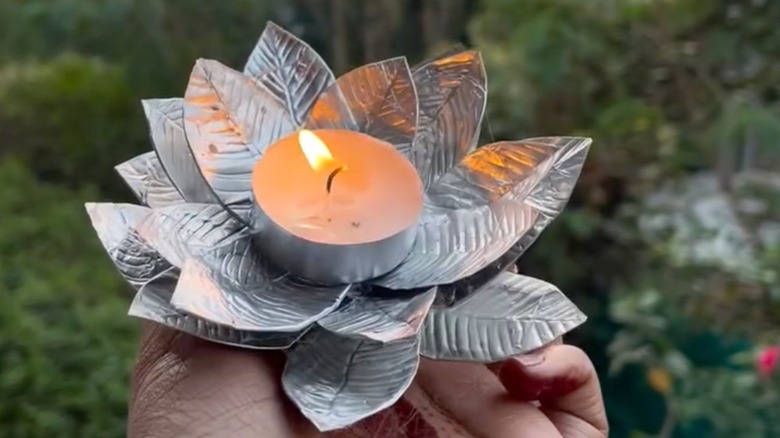 person holding DIY candle holder made of tea light tins with a light candle in the center
