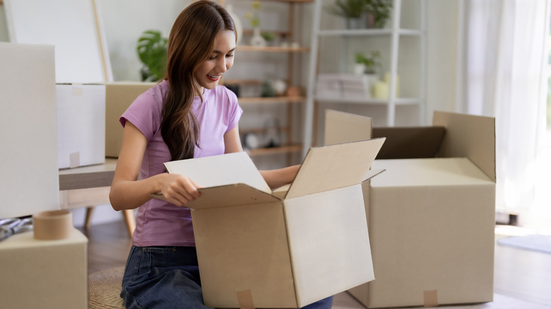 Woman holding a cardboard box sitting on the floor surrounded by boxes.