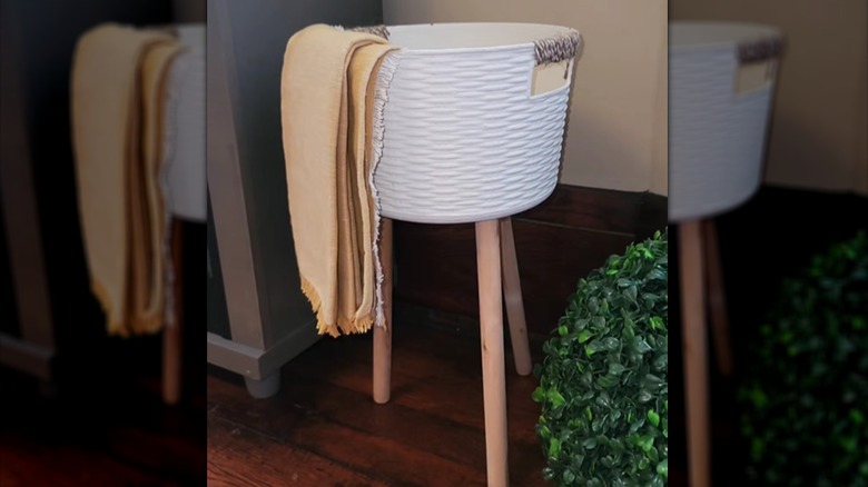 A Dollar Tree basket attached to wooden plunger handles as legs holds a blanket.