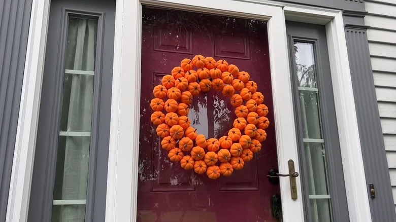 A wreath made of mini orange pumpkins hangs on a front door.