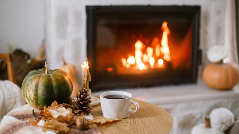Pumpkins, leaves, and a warm beverage in front of a glowing fireplace