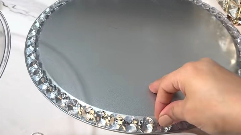 Person applying acrylic gems to Dollar Tree pizza pan to make DIY cake stand