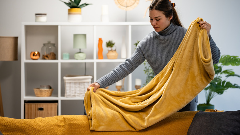 Woman folding a throw blanket in the living room.