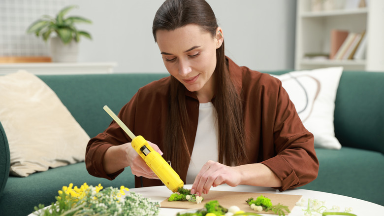 A person using a hot glue gun for crafting on a table in front of a green sofa