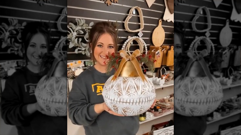A woman holding an oversized Christmas bulb made from Dollar Tree items