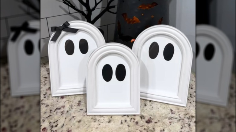 A trio of white ghosts made from Dollar Tree picture frames sit on a kitchen counter.