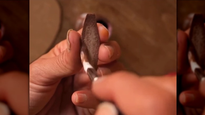 A woman painting bunny ears on an egg carton piece.