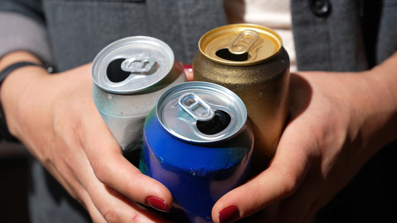 Close-up of a woman's hands holding three empty soda cans
