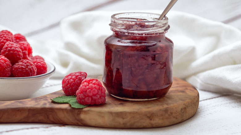 Jar of raspberry jelly and fresh raspberries on a cutting board