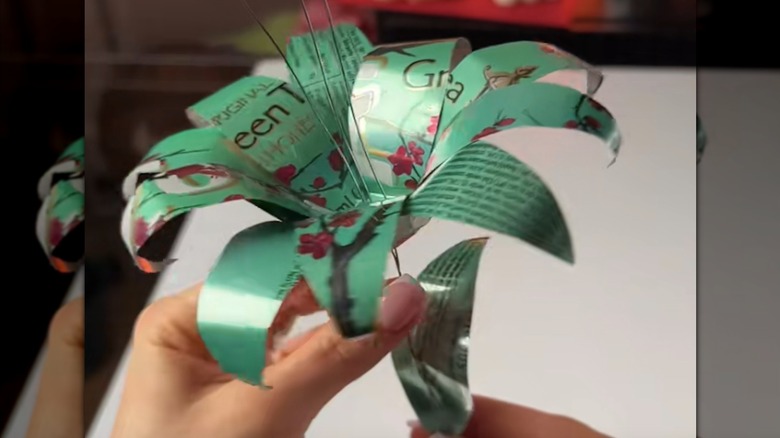 A person holding a lily flower made out of a soda can