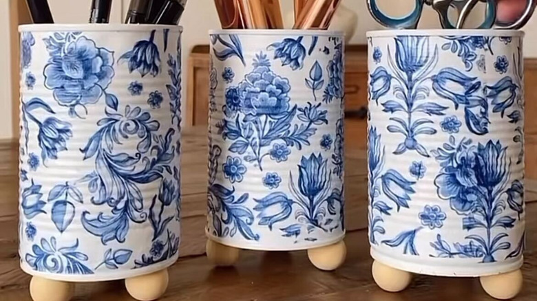 Three cans decorated in a floral pattern with wooden feet