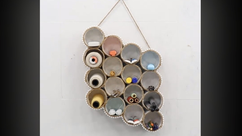 A set of tin cans are arranged like cubbies as a hanging wall ornament, each filled with craft goods.
