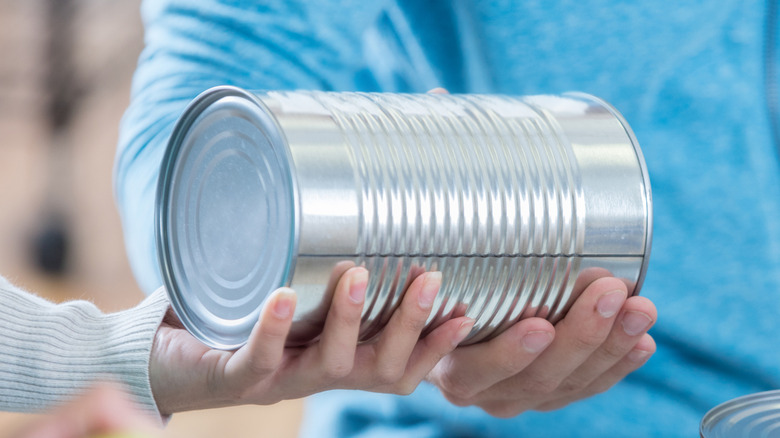 Someone holding a silver, ringed tin can