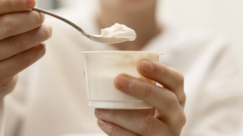 Hand scooping out a spoonful of yogurt from a small yogurt cup