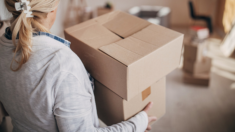 A woman carrying a stack of cardboard boxes indoors