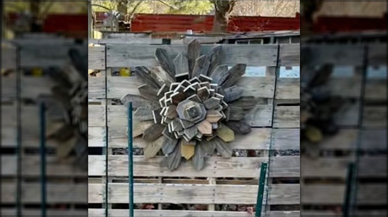 A flower made from weathered wood hangs on a wood pallet.