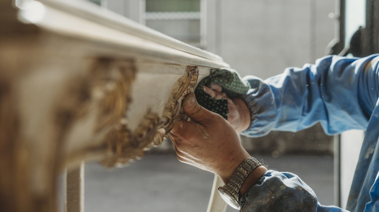 A hand polishes wooden ornamentation on a table.