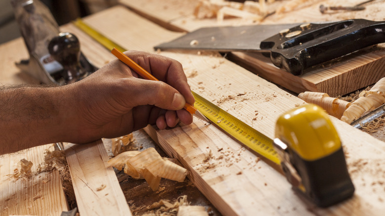 Person marking a piece of lumber with a pencil