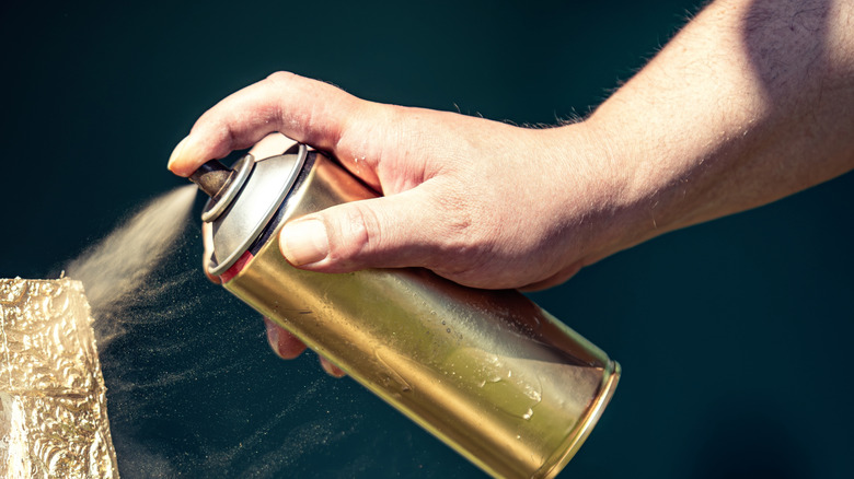 A hand spraying gold spray paint onto a frame