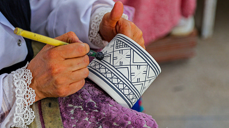 An artisan carefully painting geometric patterns on a handmade Morrocan cup.