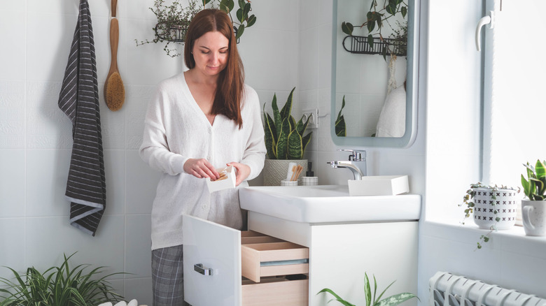 A woman declutters the drawers in the vanity of a modern bathroom.