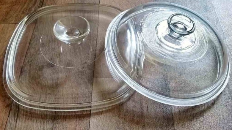 Two transparent glass casserole dish lids sit on a wooden countertop.