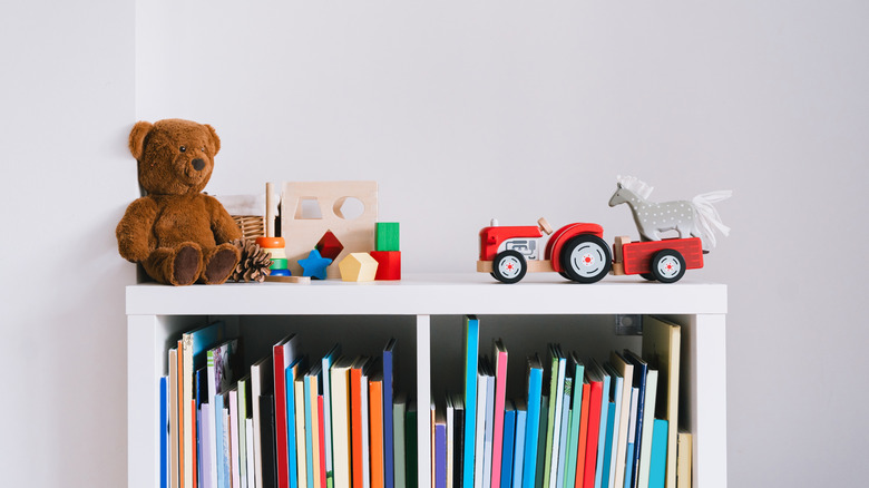 Children's books on a narrow shelf with toys atop