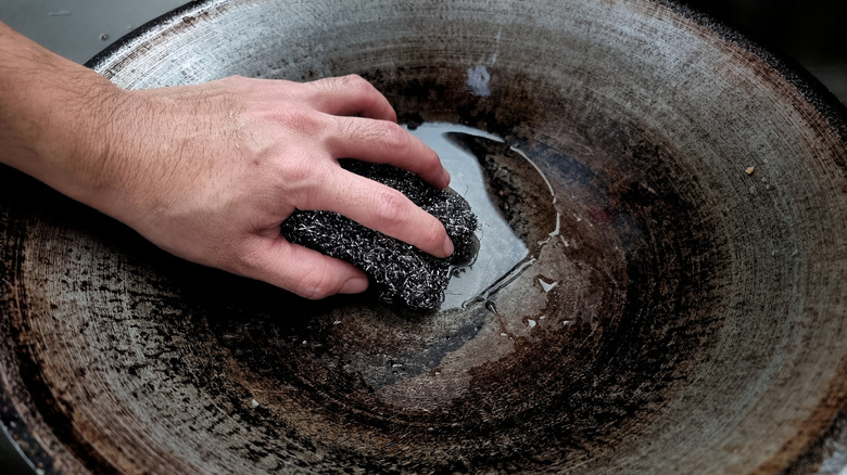 A closeup of a person scouring a dirty old frying pan.