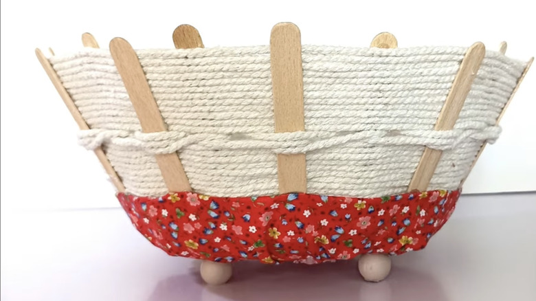 A stylish, woven basket made out of rope, fabric, popsicle sticks, and a frying pan base.